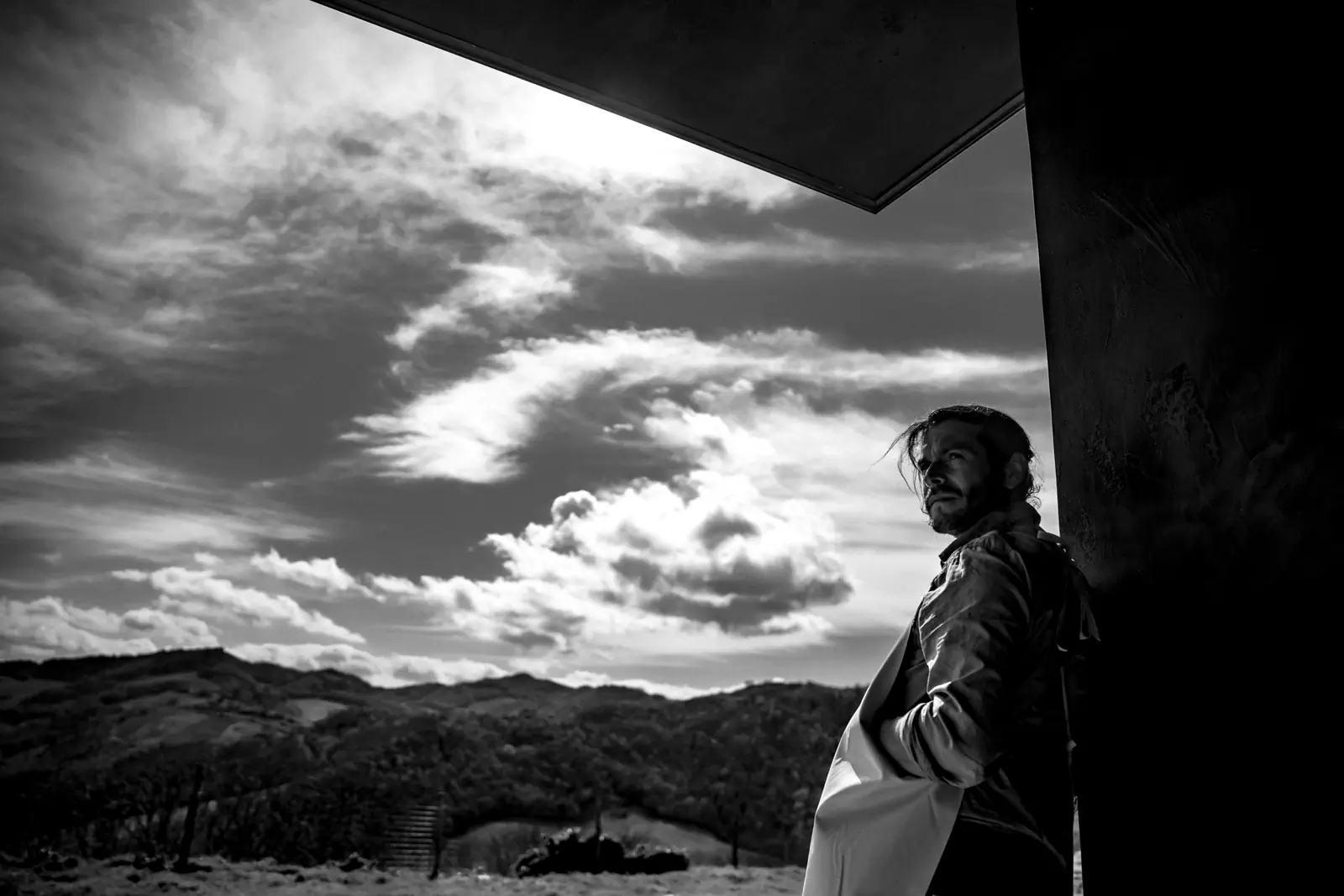 Black-and-white shot of a man under a dramatic cloudy sky over hills