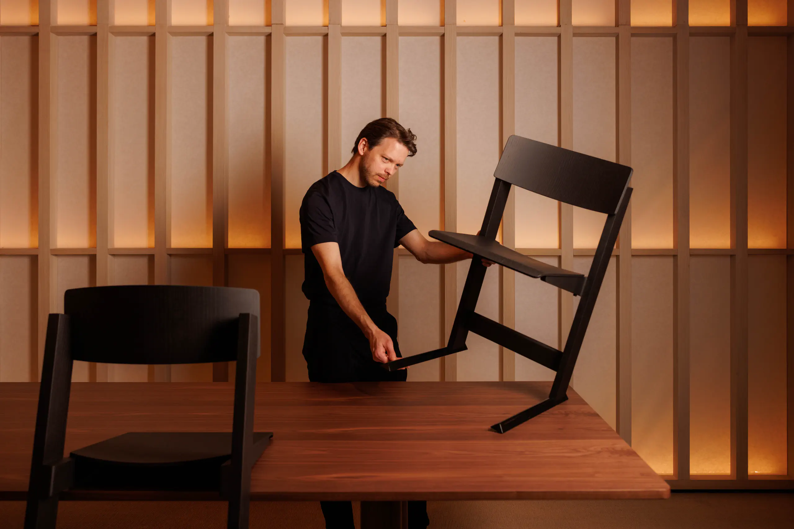 Man holding a chair over a table in a warm-lit panelled room