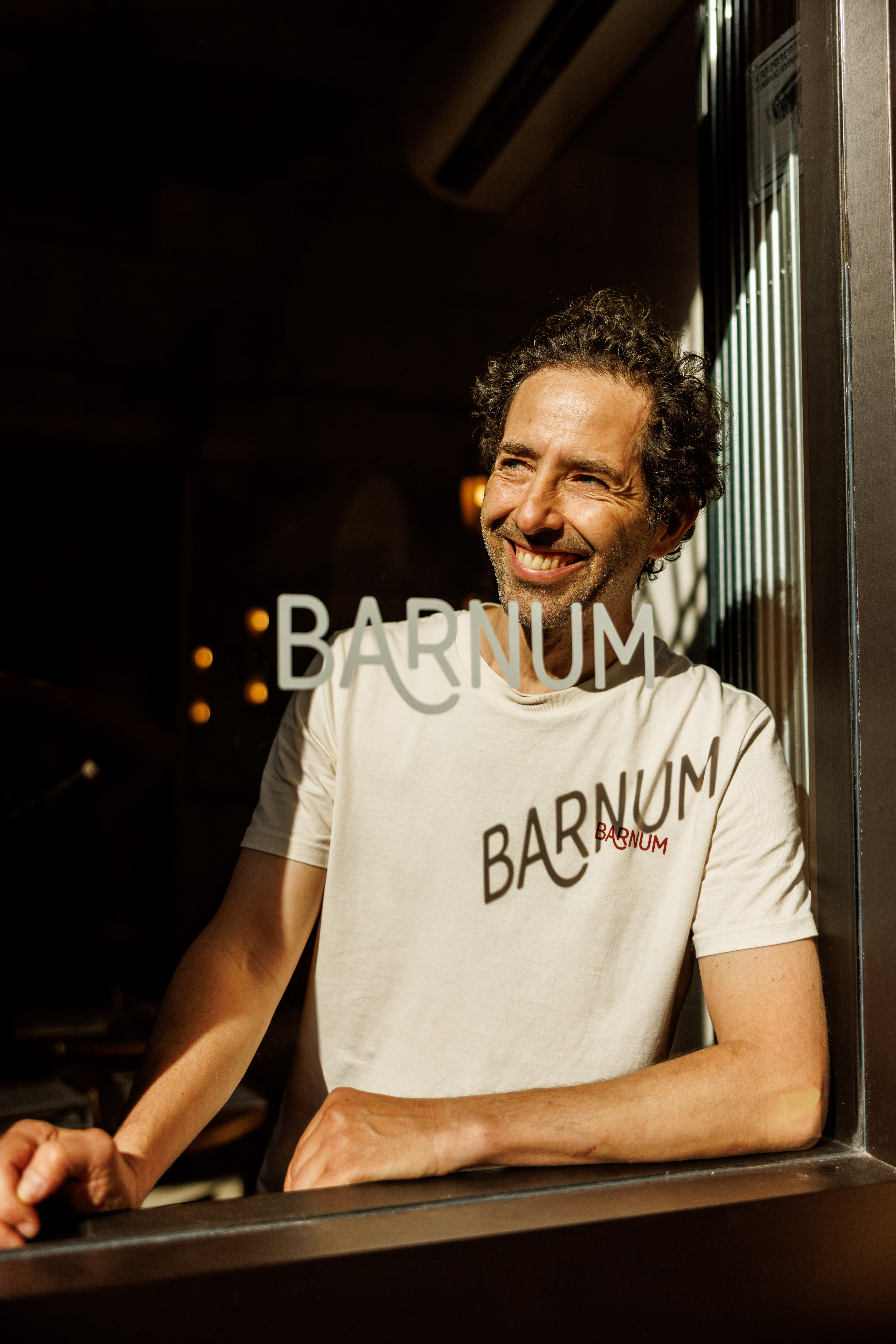 Man in a 'Barnum' t-shirt leaning at a window at night