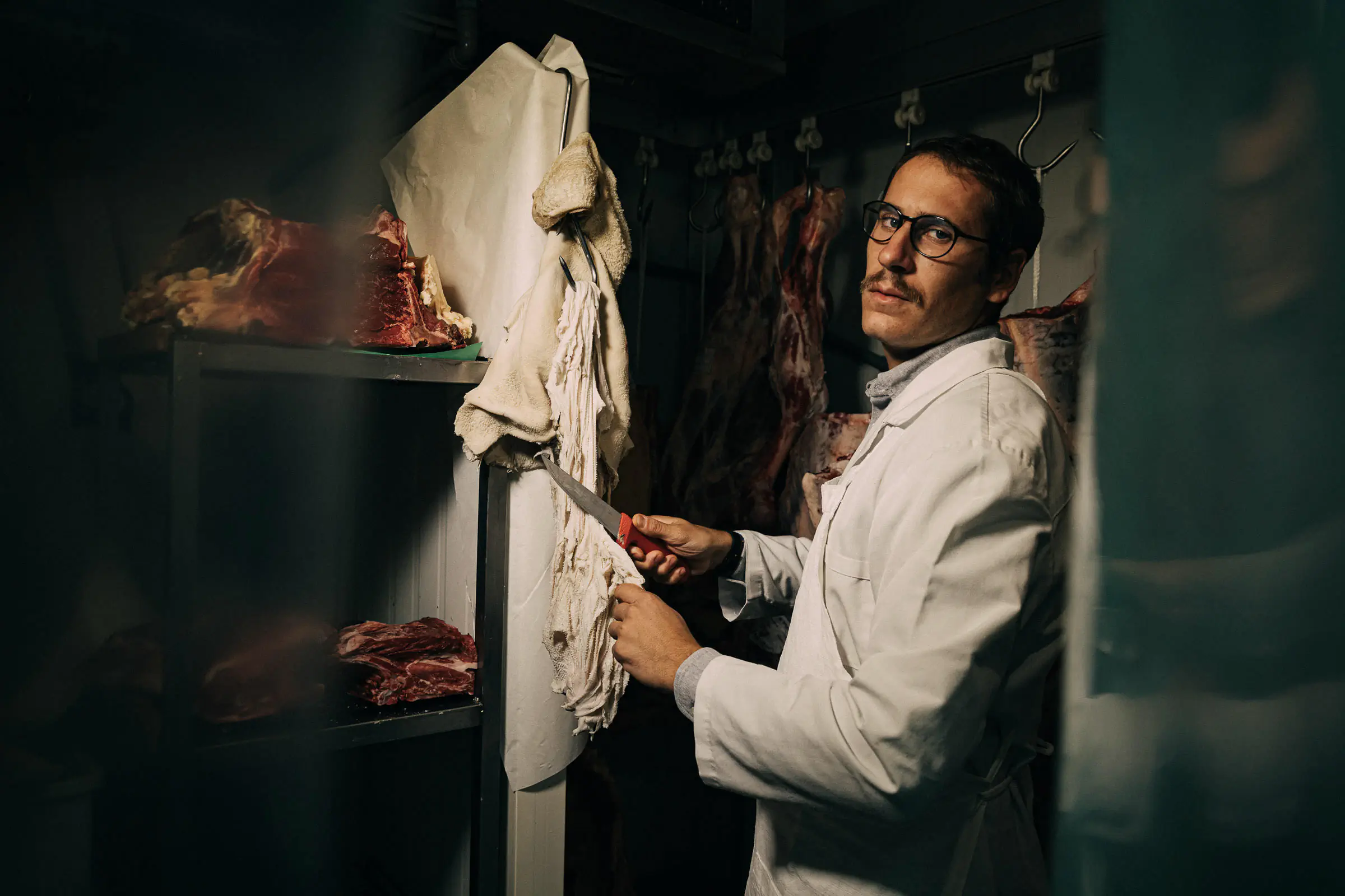 Man in whites holding a knife in a meat-aging cellar