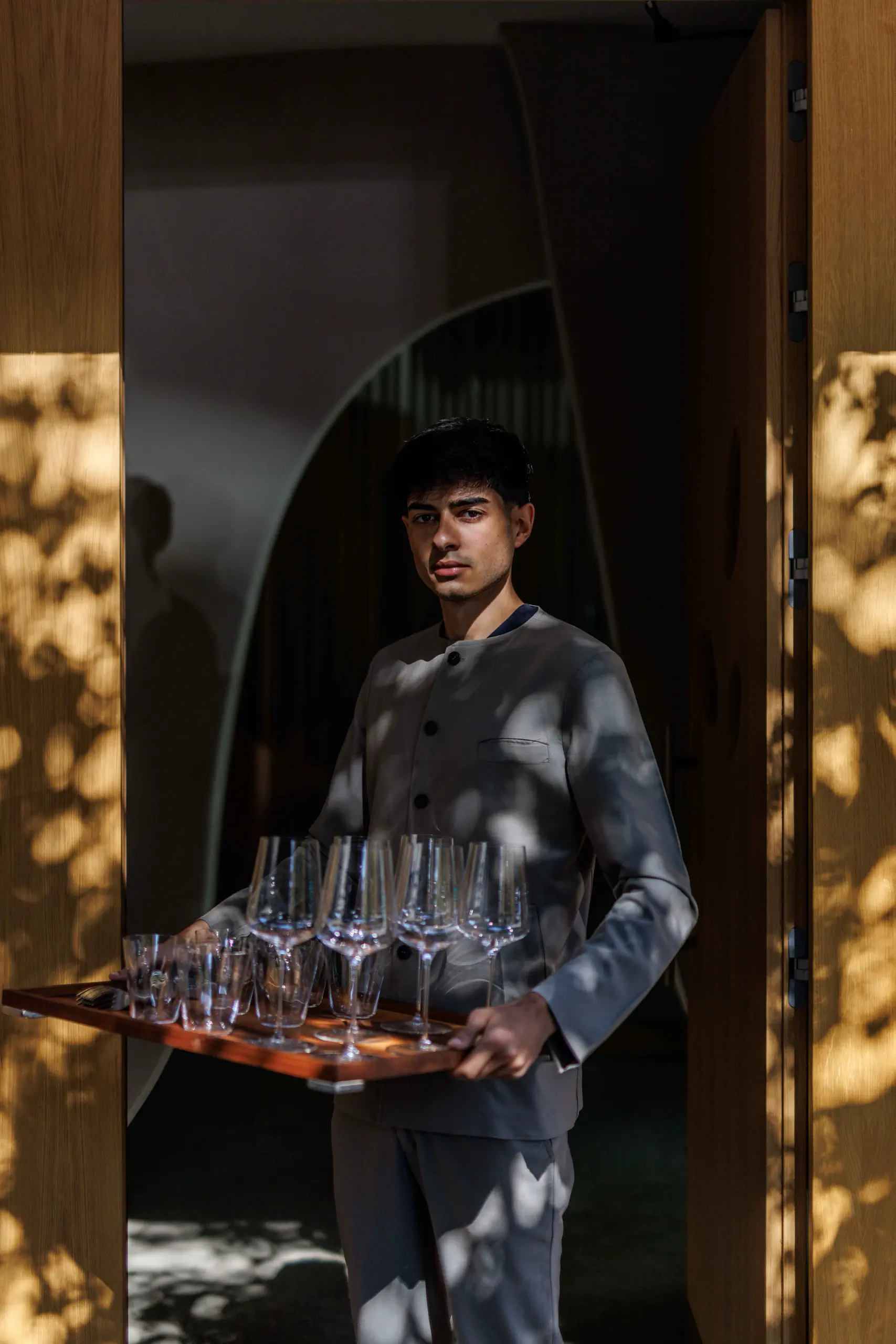 Waiter carrying a tray of glasses through a sunlit doorway