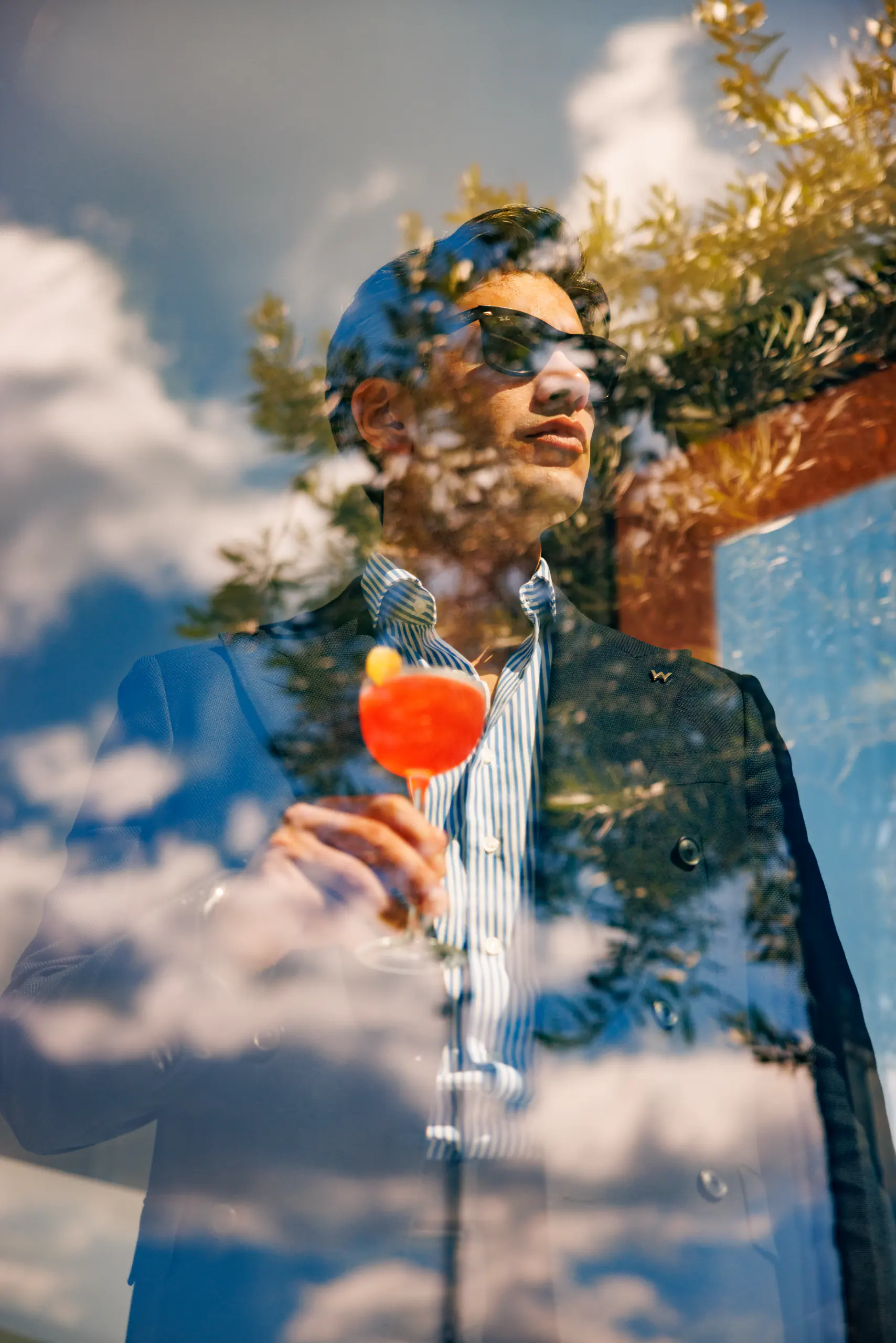 Double-exposure portrait blending a man's face with a cocktail and sky