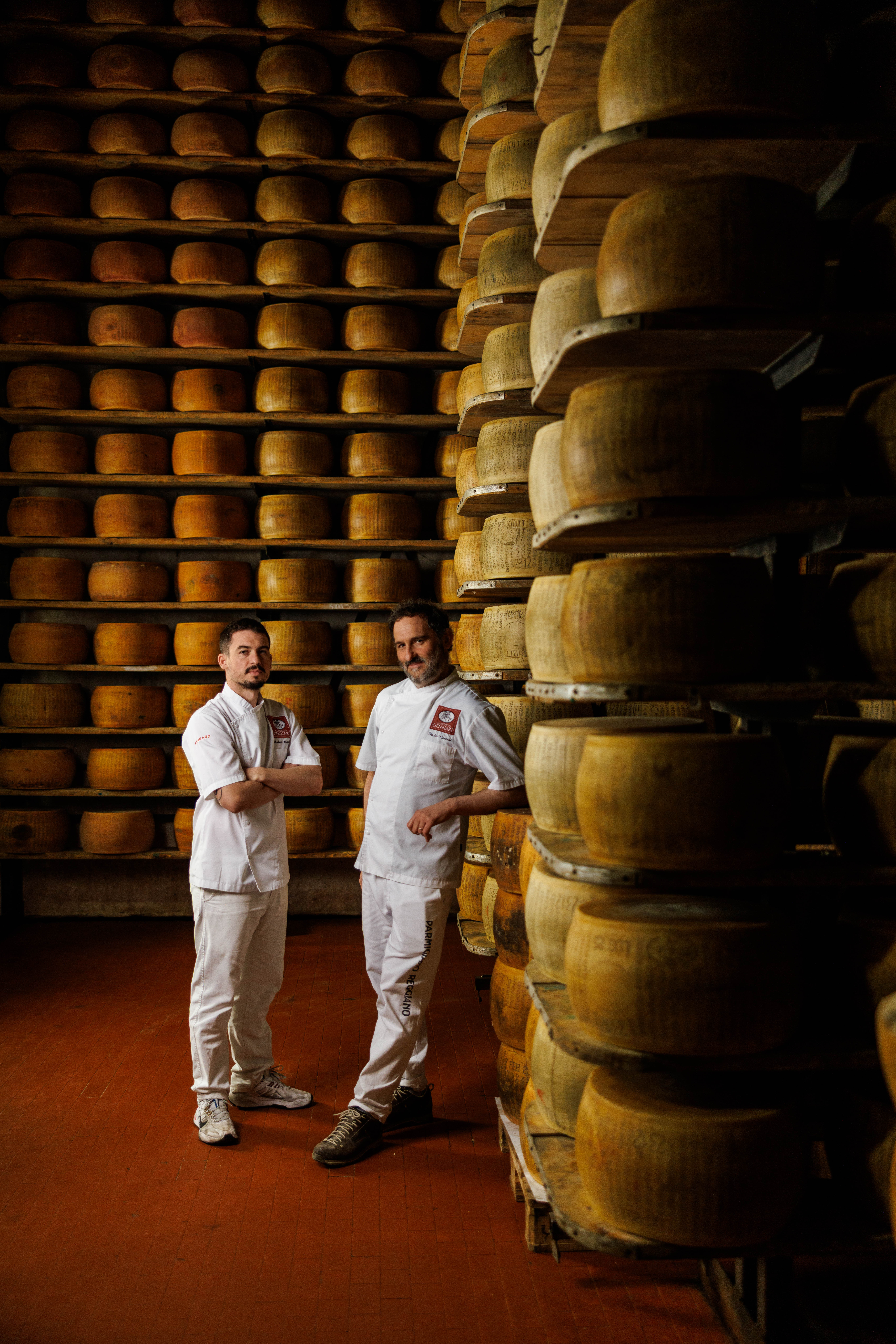 Two people among towering stacks of aging cheese wheels
