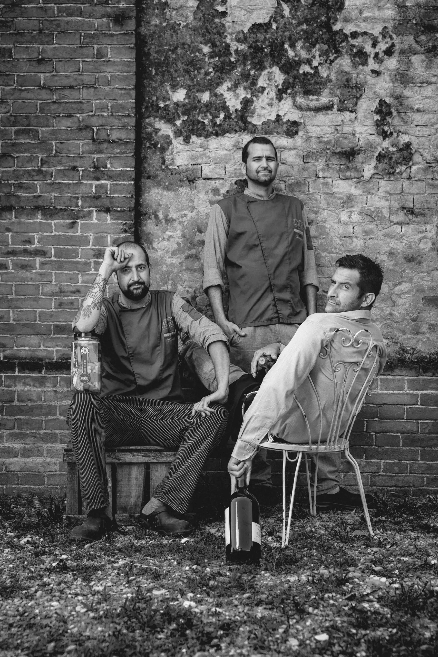 Black-and-white group portrait of three people against a stone wall