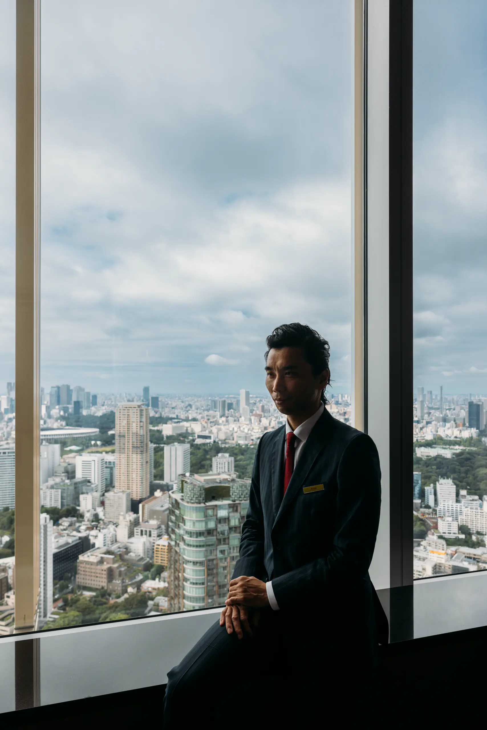 Man in a suit seated by a large window overlooking a city skyline