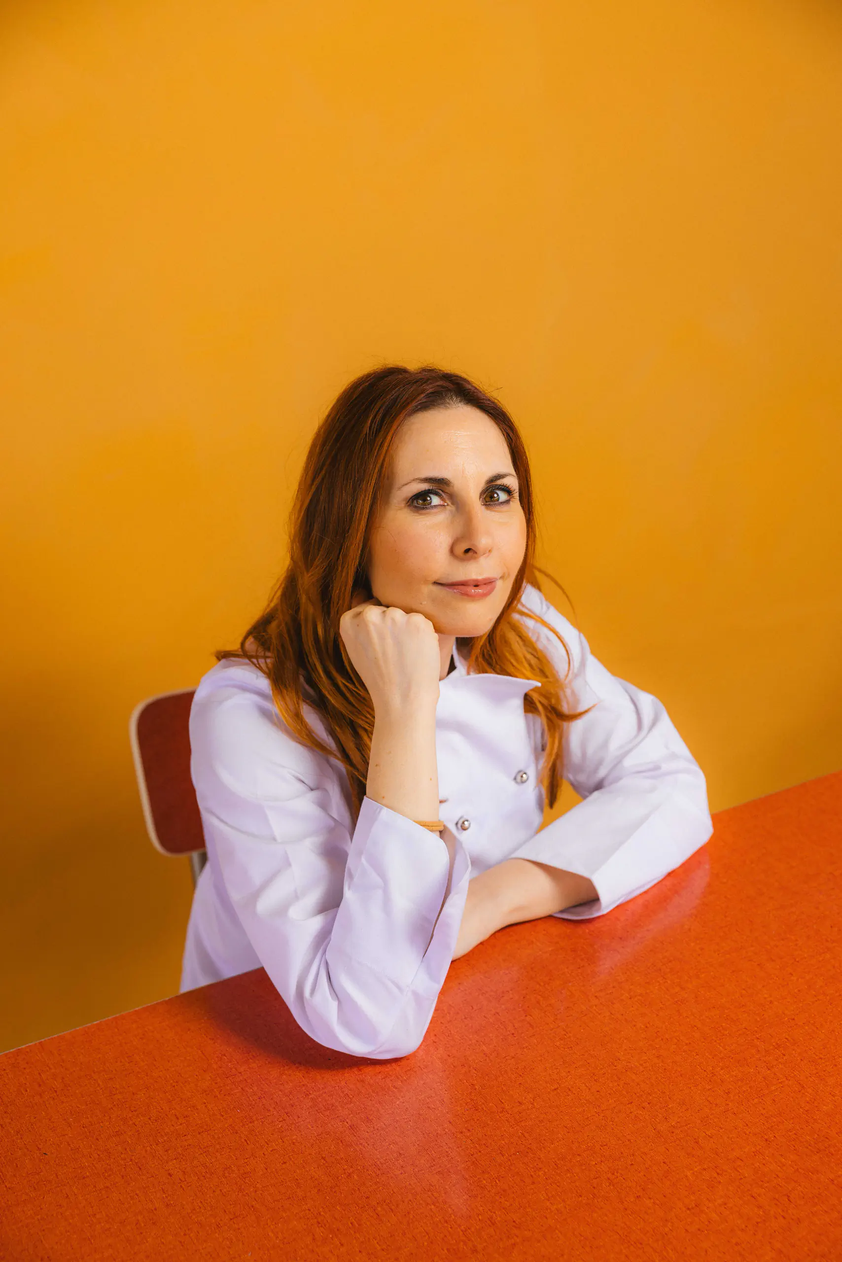 Woman resting her chin on her hand against an orange background
