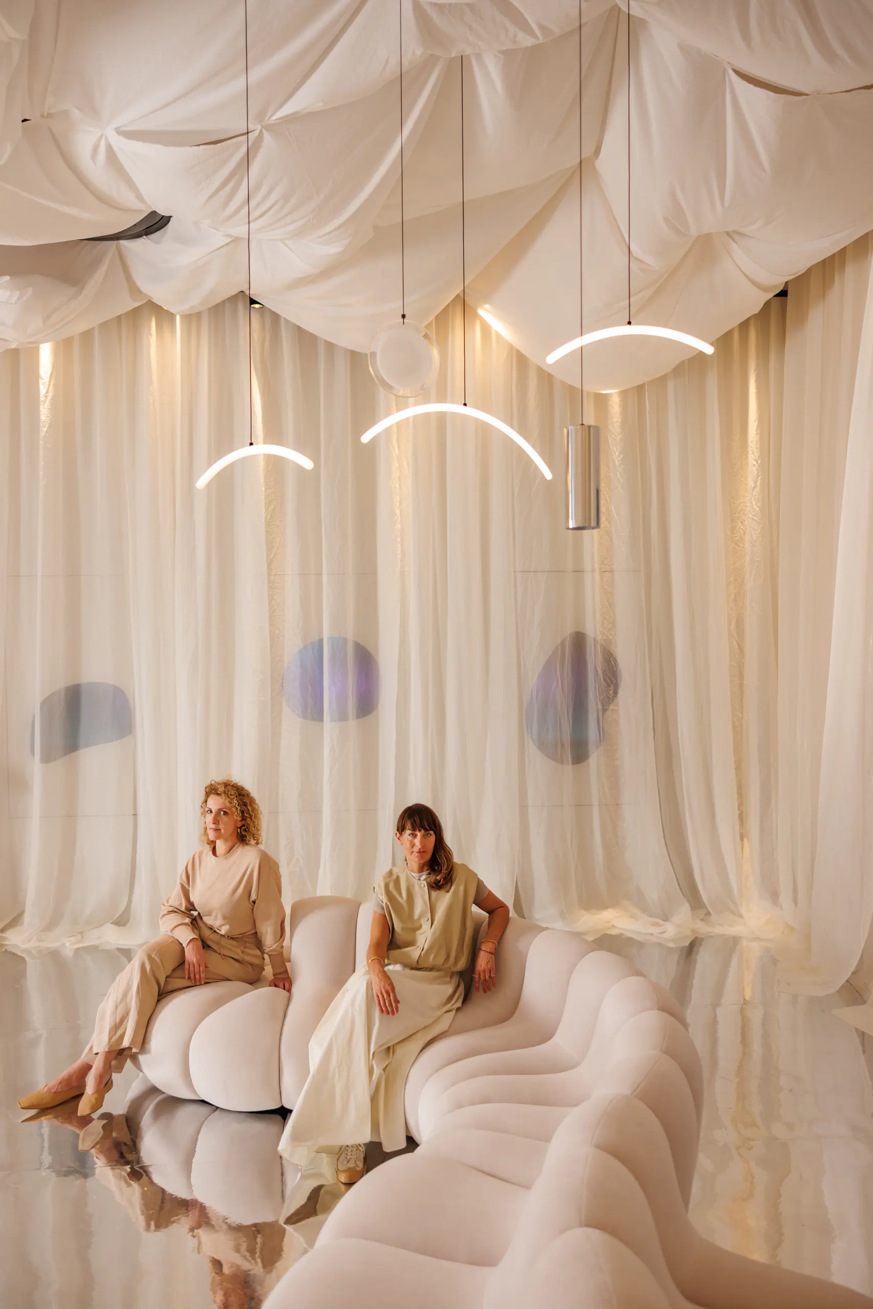 Two people seated on a draped daybed in an ethereal curtained setting