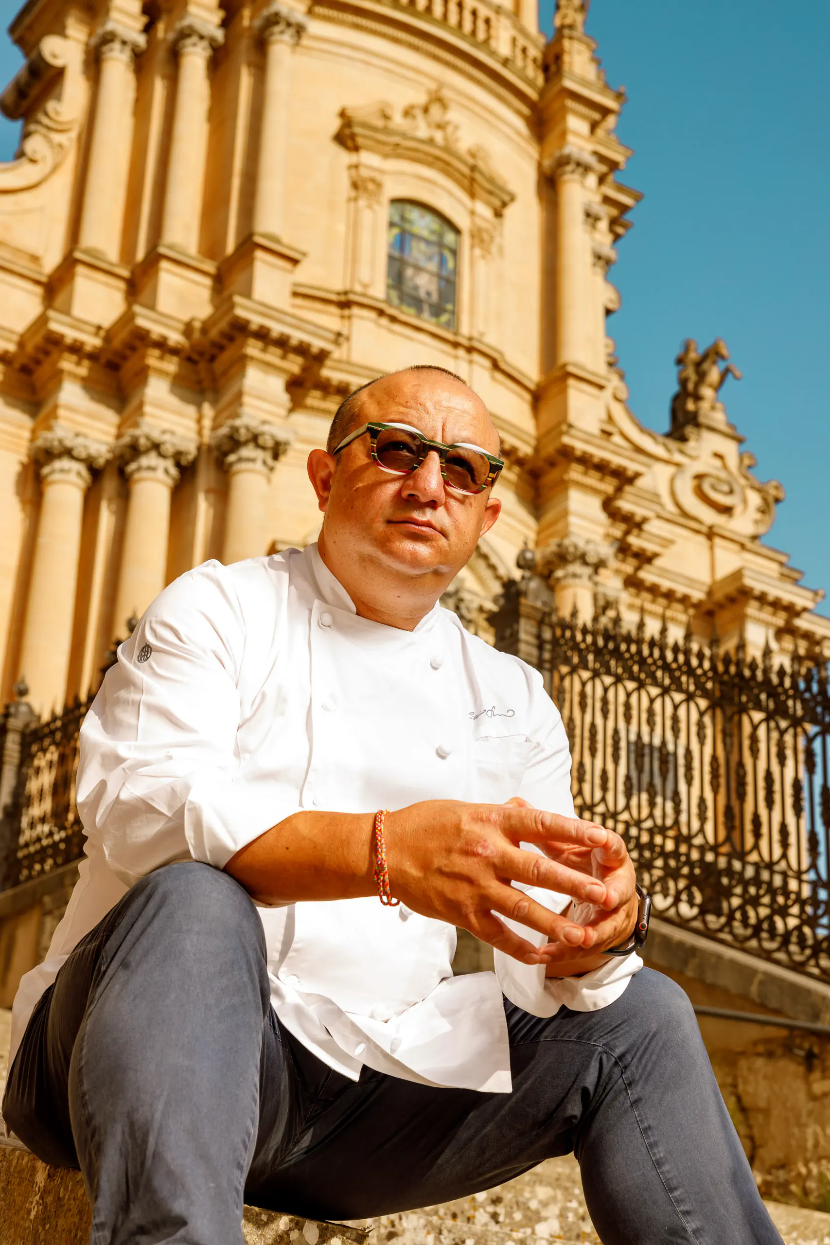 Chef in whites and sunglasses seated before an ornate Baroque church facade