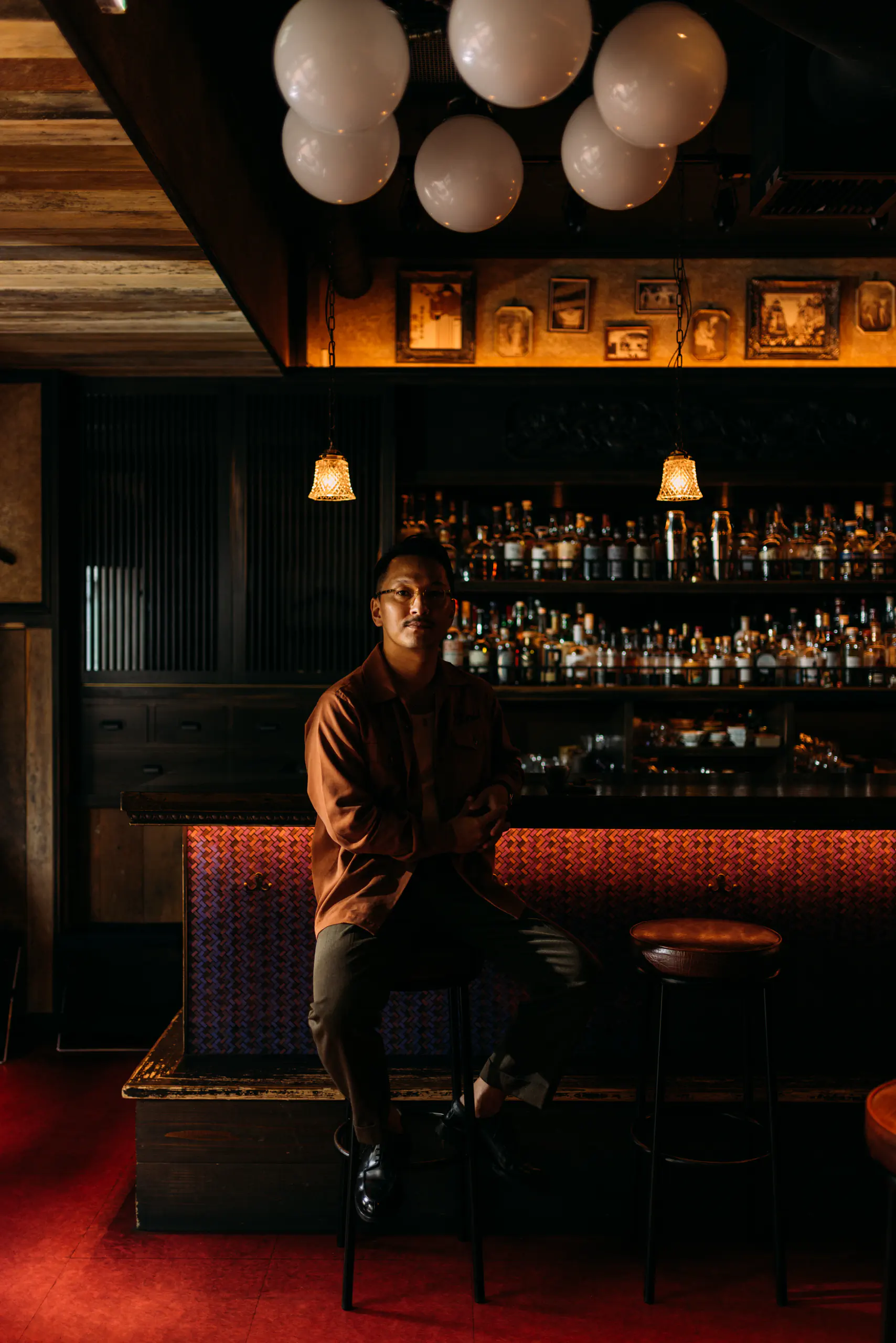 Person seated at a dark moody bar with warm-lit bottle shelves