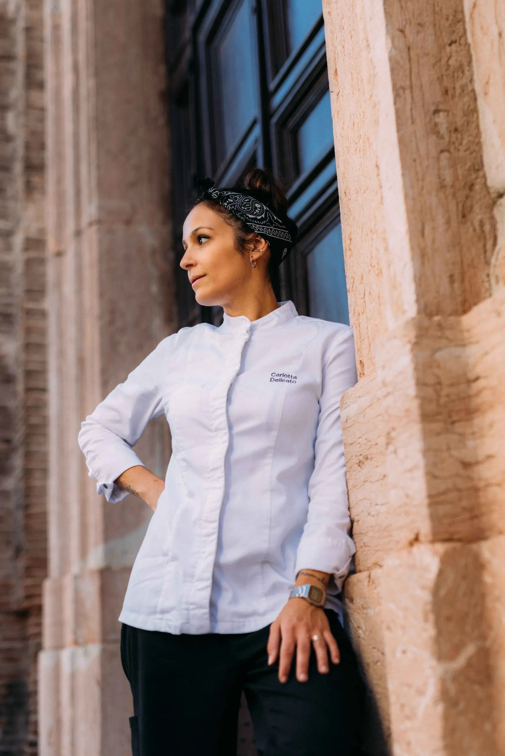 Woman in a white chef's jacket leaning against a stone column