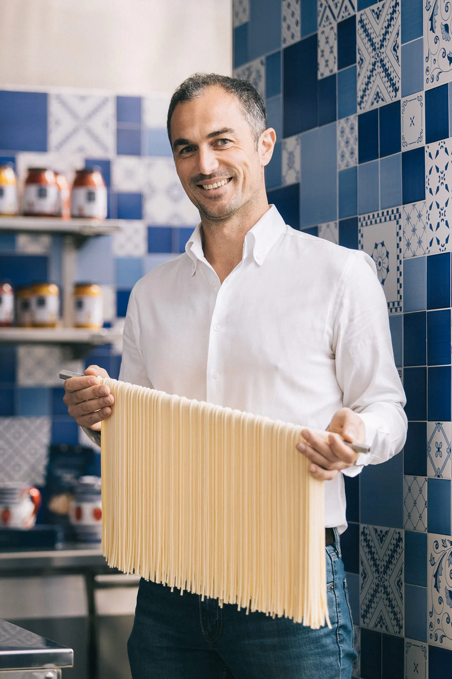 Smiling man holding a sheet of fresh pasta in a tiled kitchen