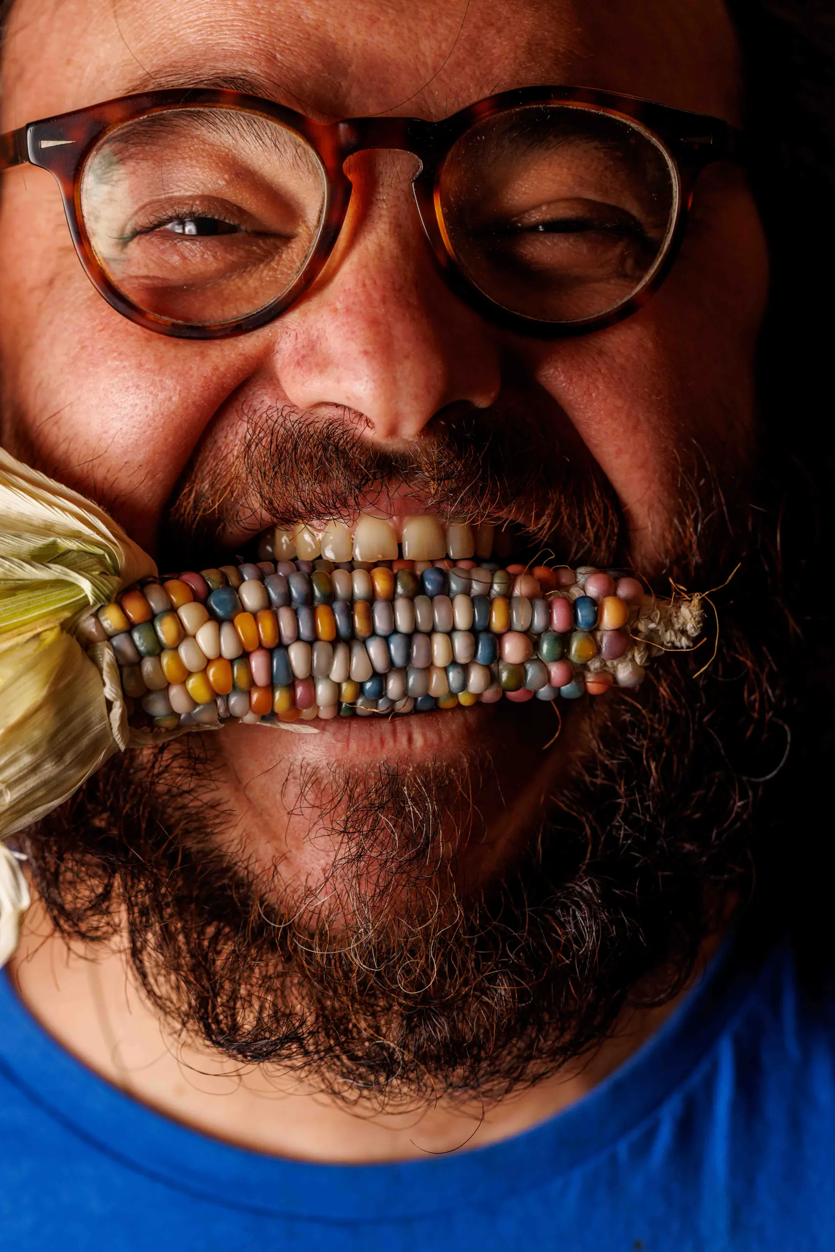 Close-up of a smiling bearded man biting into multicoloured corn