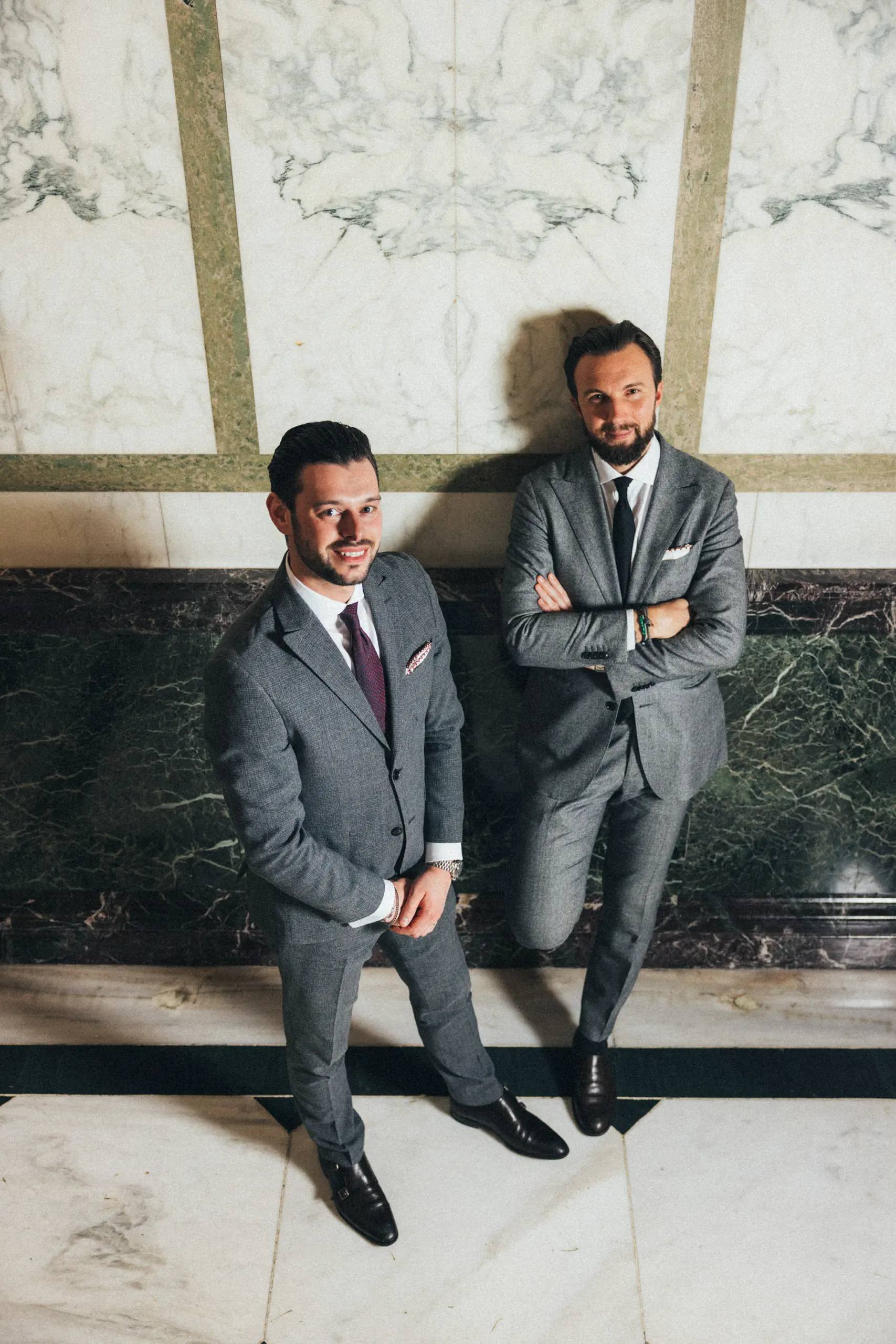 Two men in suits seated against a marble wall