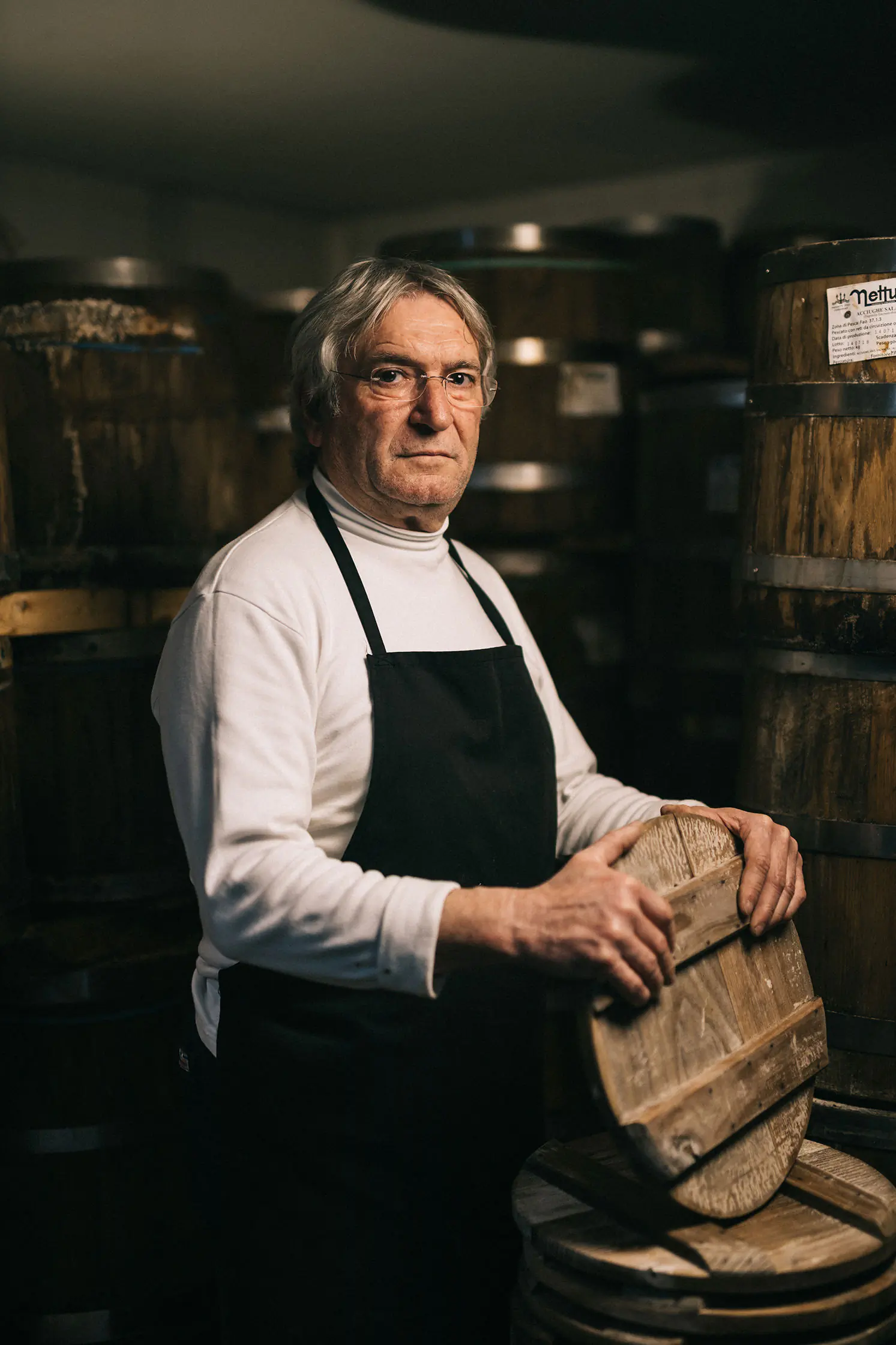 Man in an apron seated on a wine barrel in a dark cellar