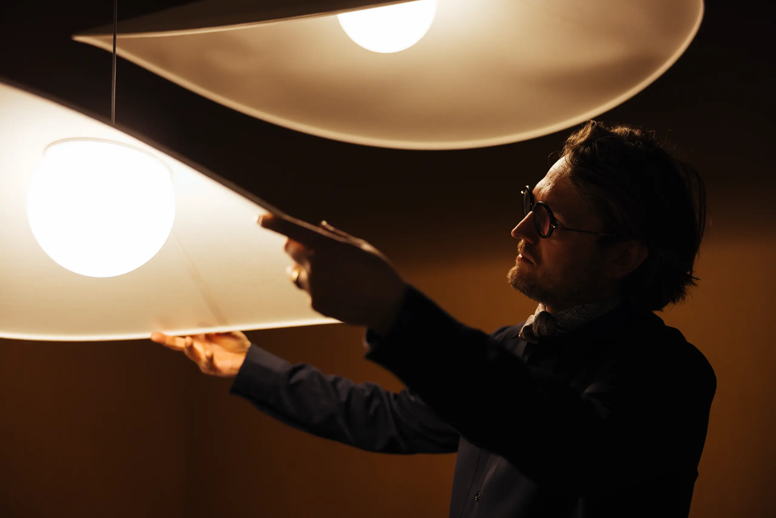 Man adjusting a large glowing pendant lamp