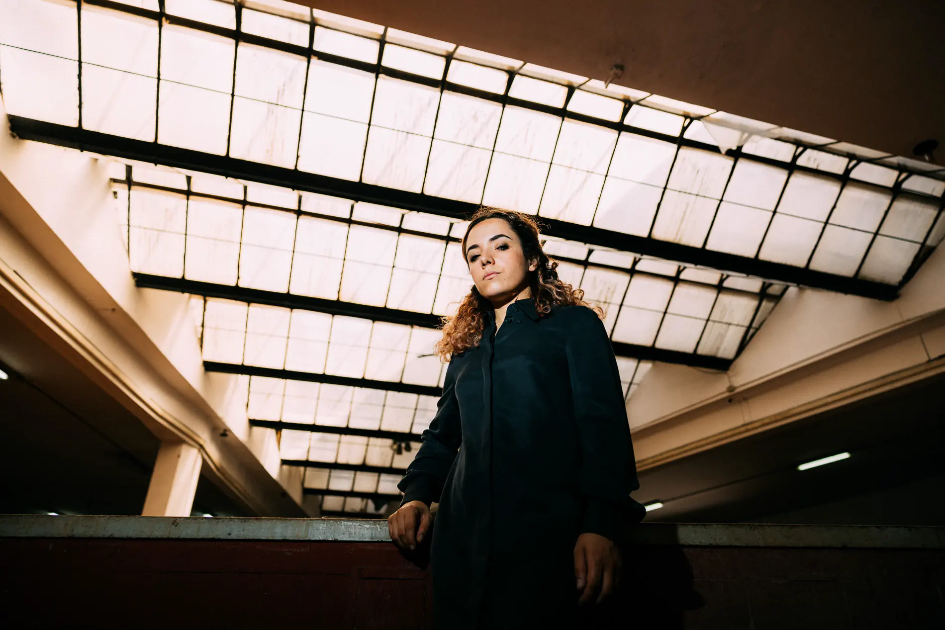 Woman in a dark coat under a large industrial glass roof