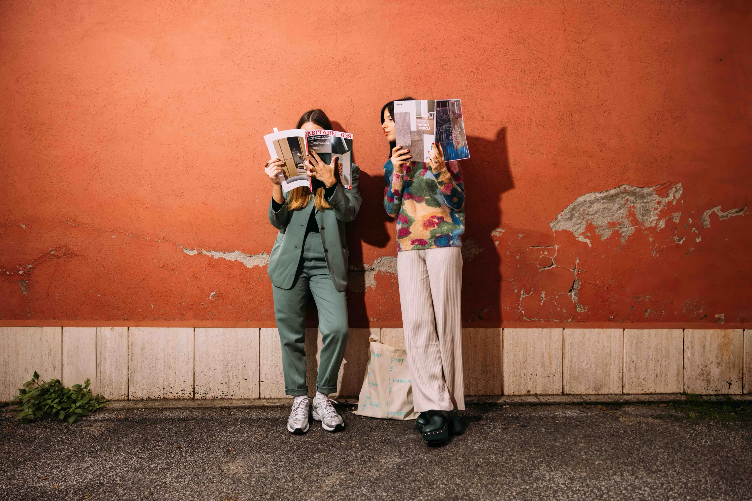 Two people holding open magazines in front of their faces against a red wall