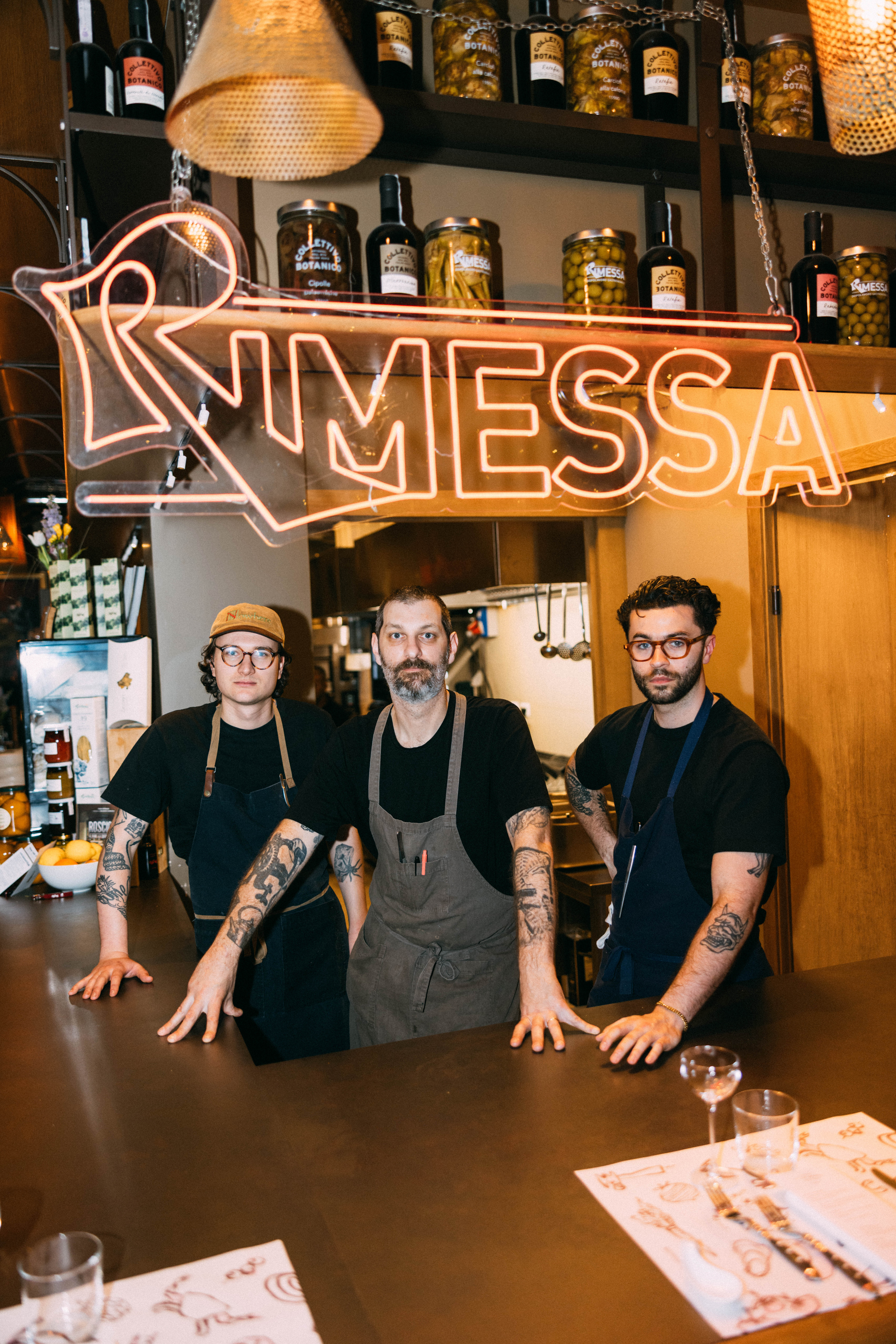 Three staff members behind a bar under a neon sign