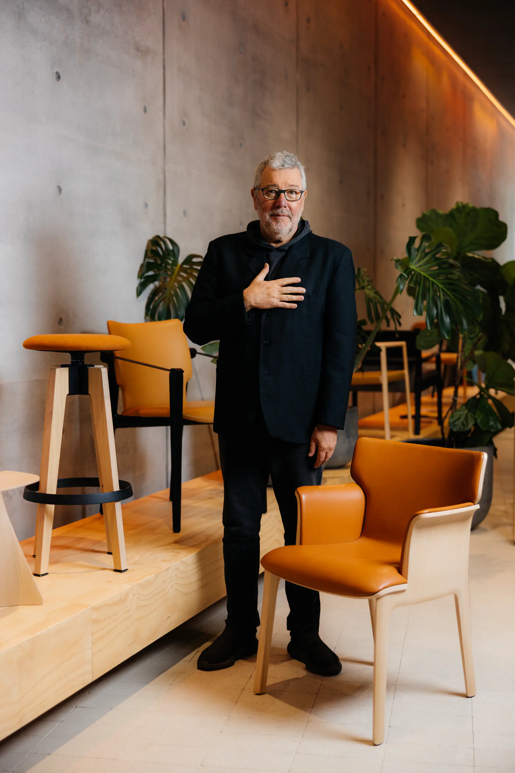 Older man in a dark coat in a design showroom with orange chairs