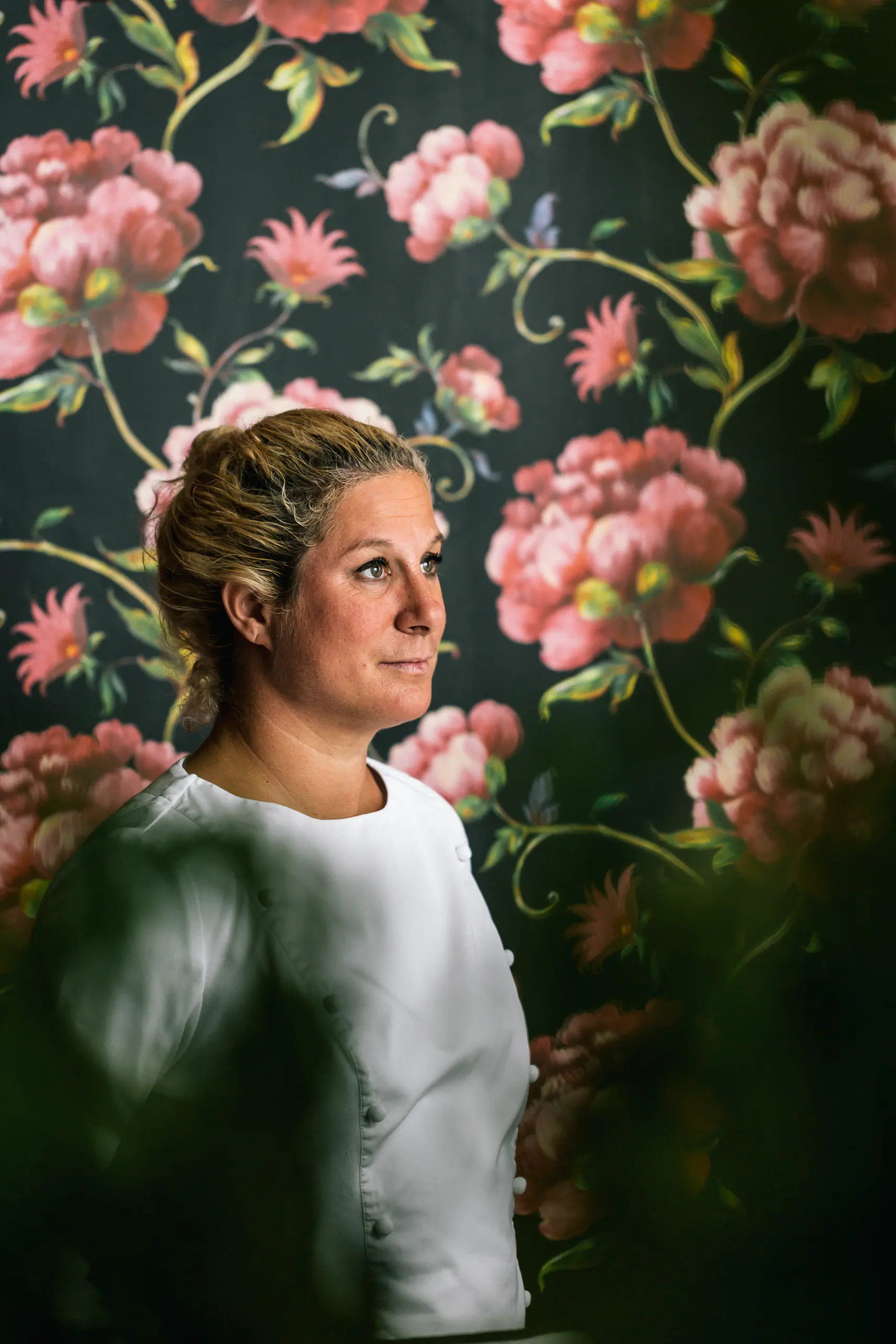 Woman with braided hair against a dark floral wallpaper backdrop