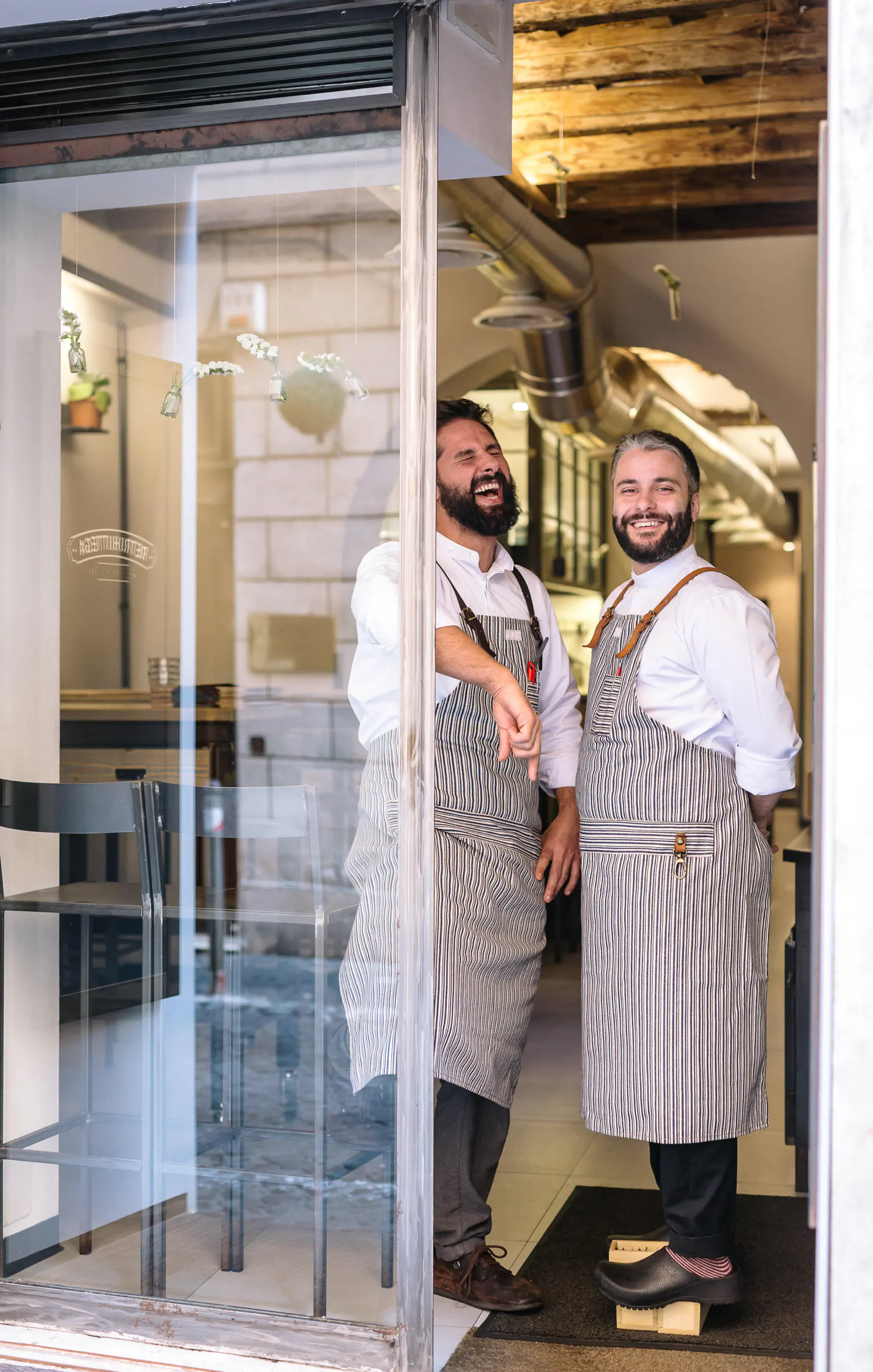 Two people in aprons in a kitchen doorway with a strip curtain