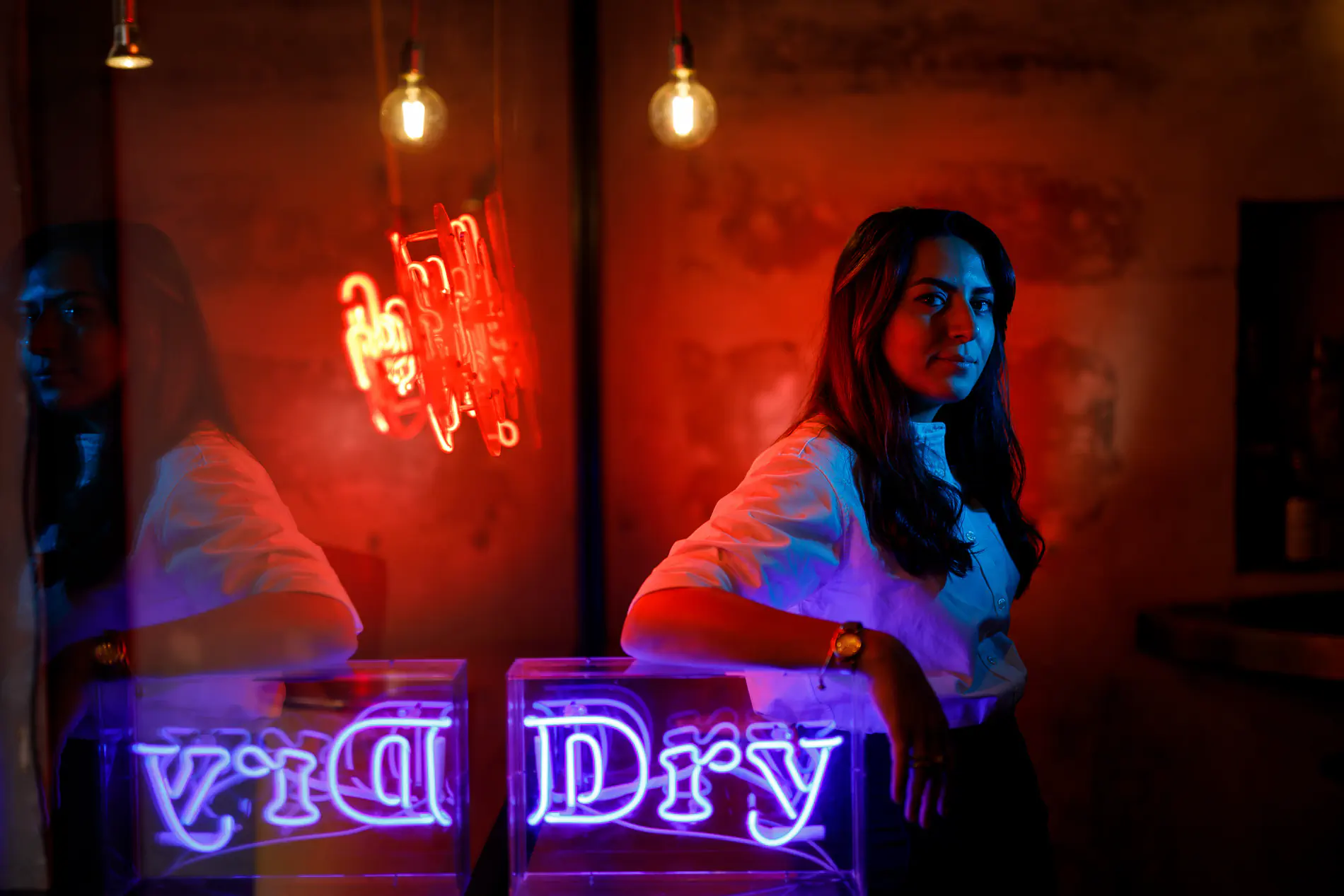 Woman leaning against a red neon-lit wall reading 'Dry'