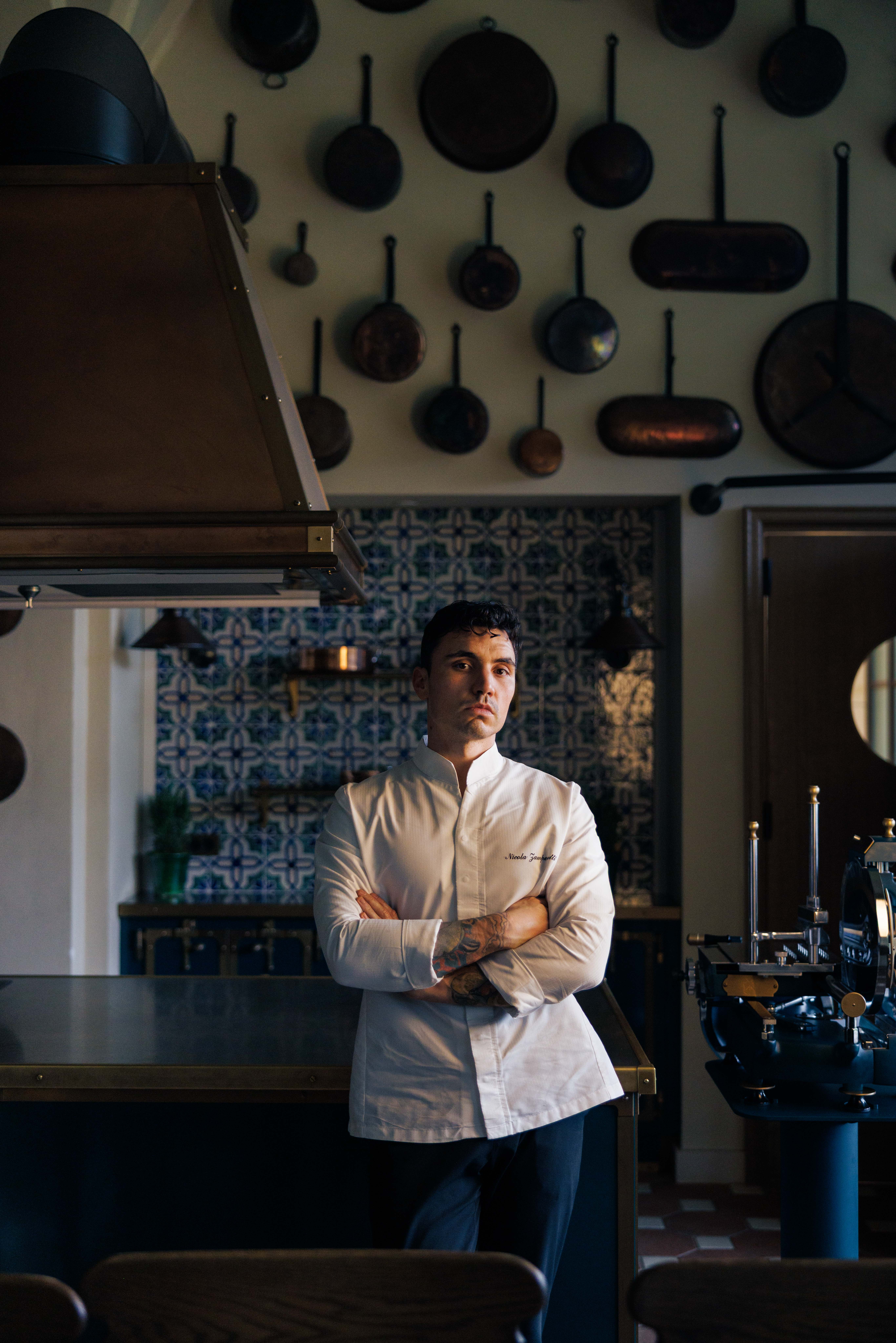 Chef in whites with arms crossed in a kitchen with hanging copper pans — Collegio alla Querce, Florence