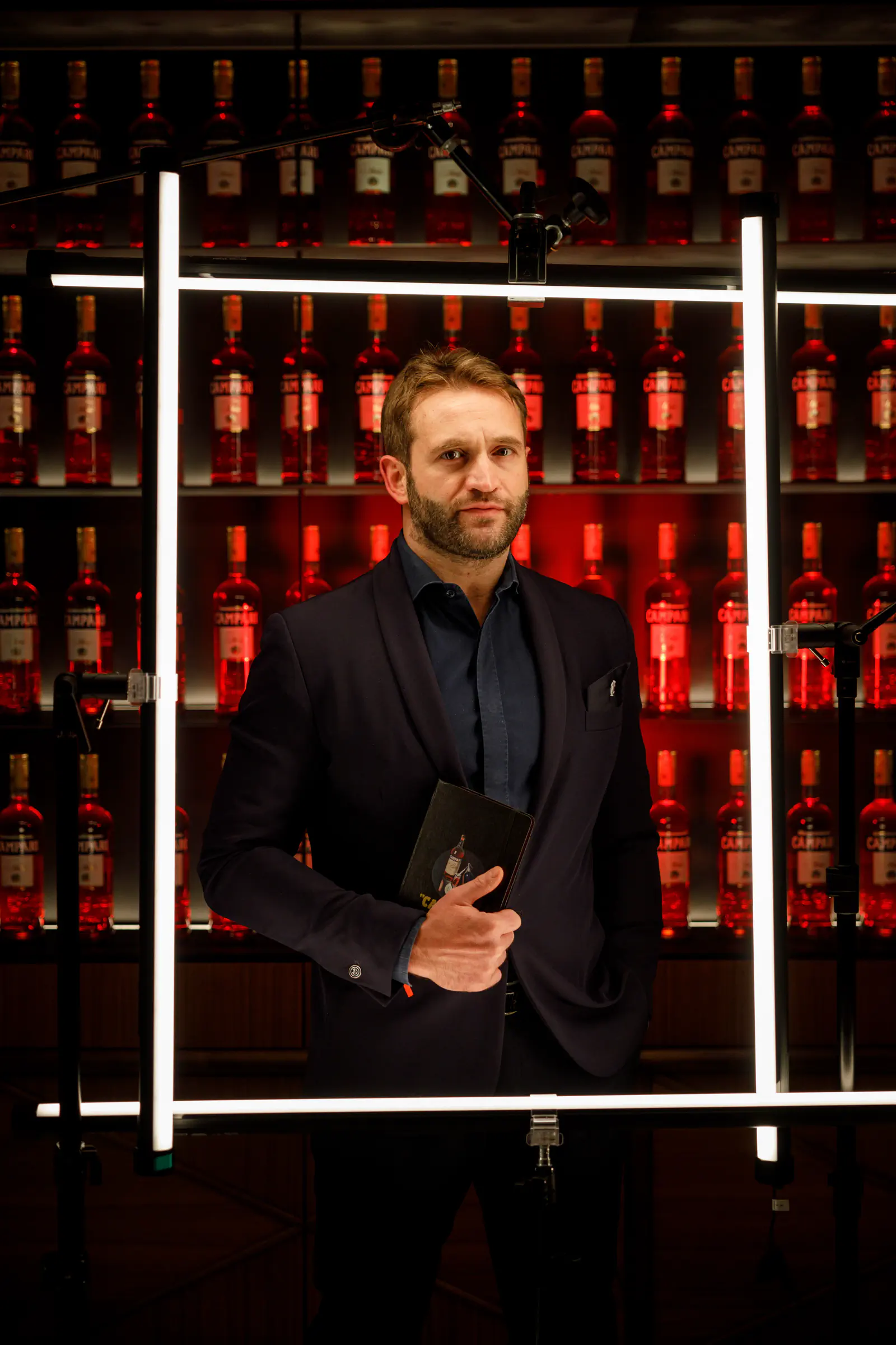 Man in black by a red-lit bar with shelves of bottles — Camparino in Galleria, Milan