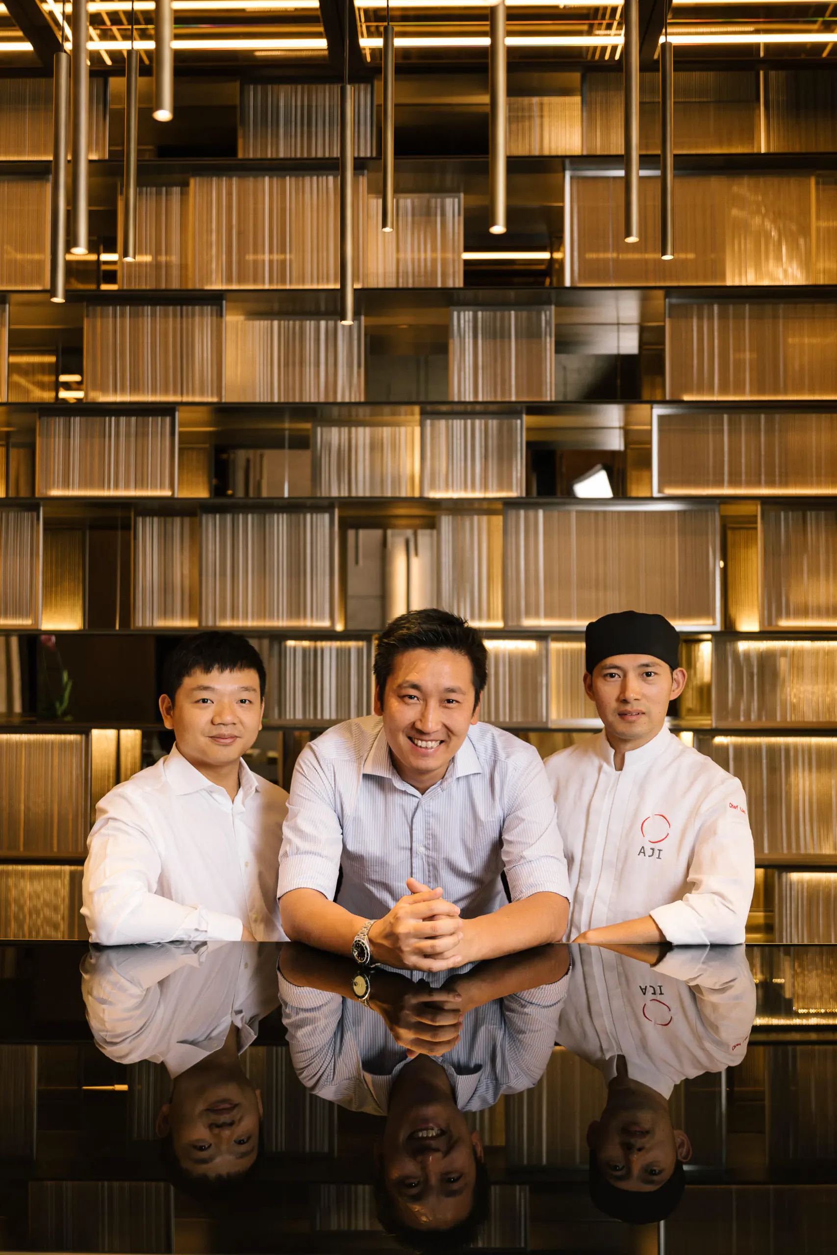 Three people in white seated at a counter before a large bookshelf