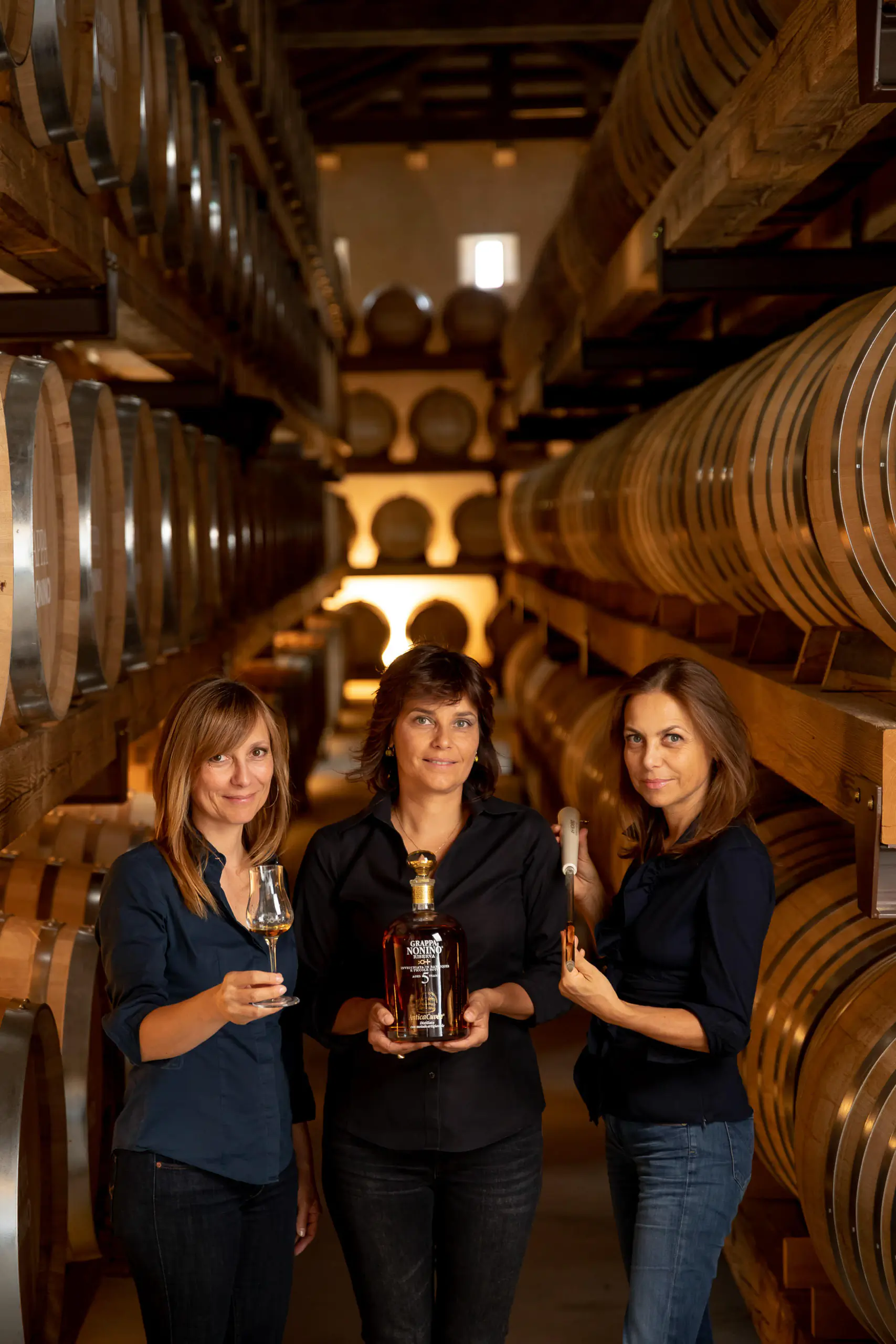 Three people holding wine in a barrel cellar