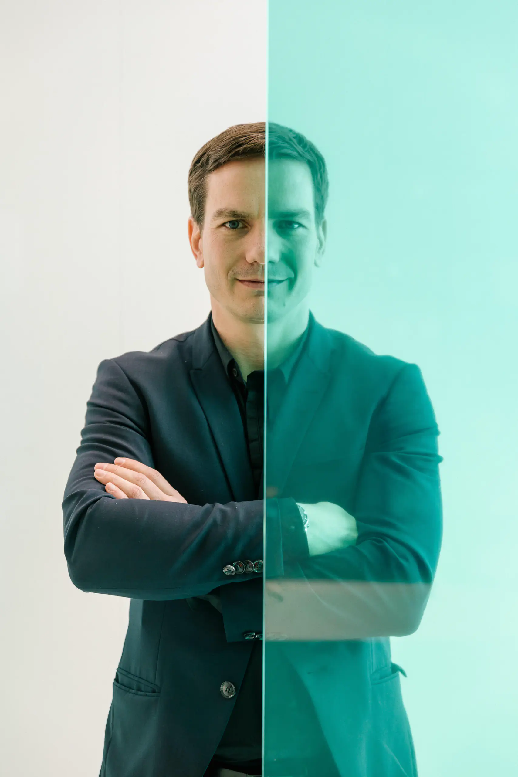 Man in a suit with arms crossed against a teal background