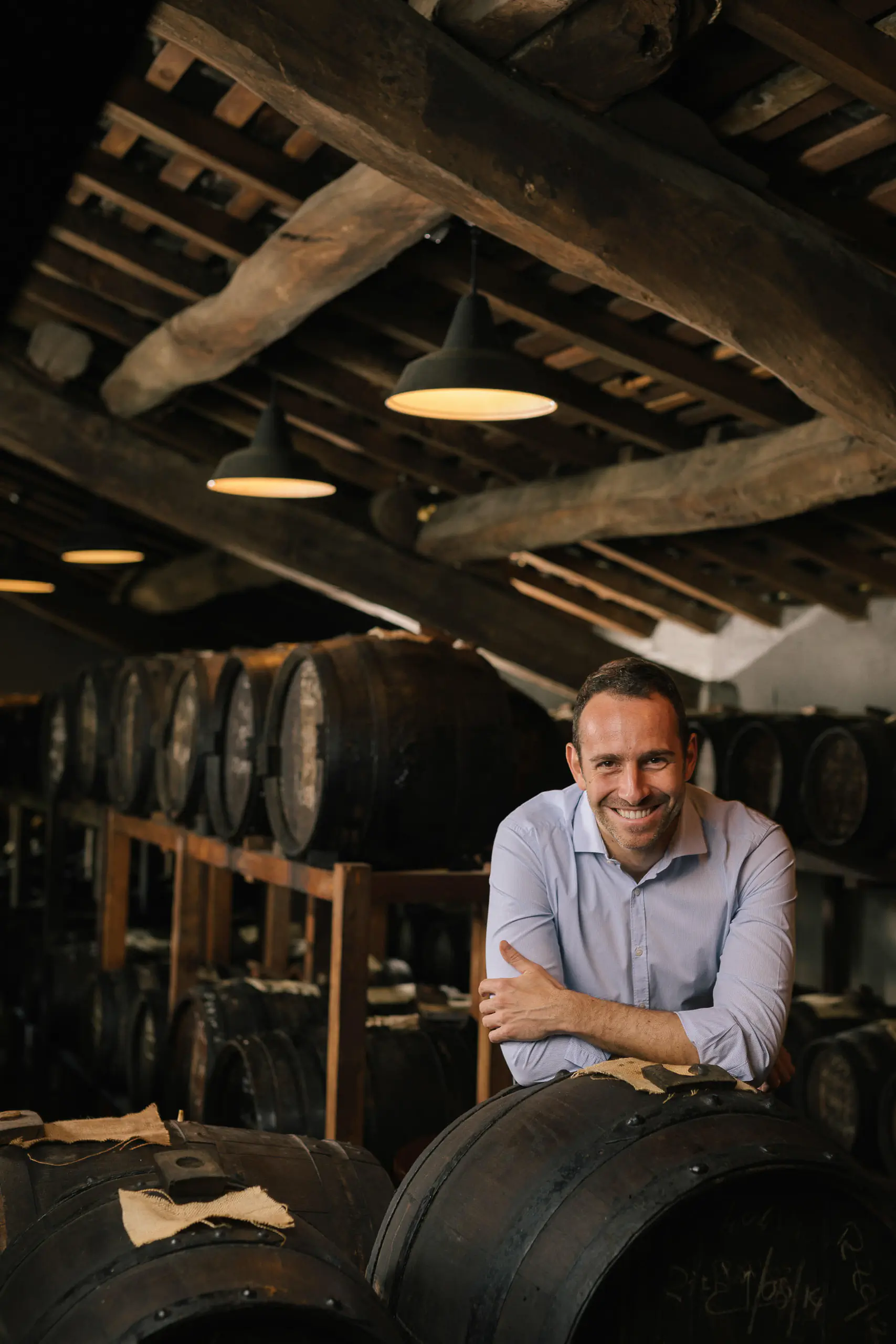 Man in a blue shirt leaning on a wine barrel in a rustic cellar