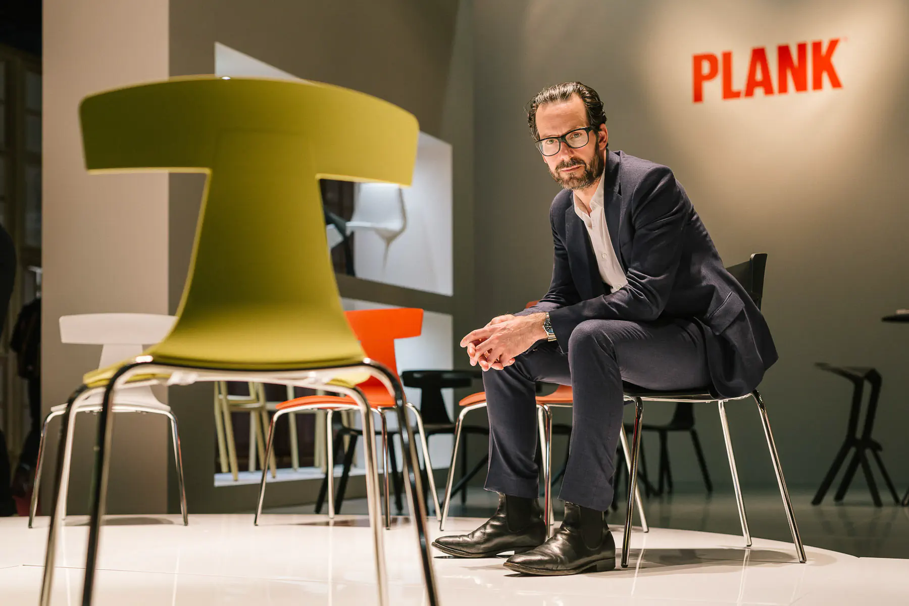 Man in a suit seated among design chairs in a showroom